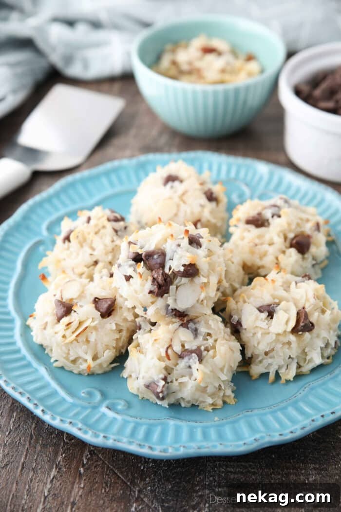 Almond Joy Cookie Recipe with Coconut, Almonds & Chocolate Chips 4 Angled view of plate of Almond Joy Macaroons with bowls of sliced almonds and chocolate chips in the background.