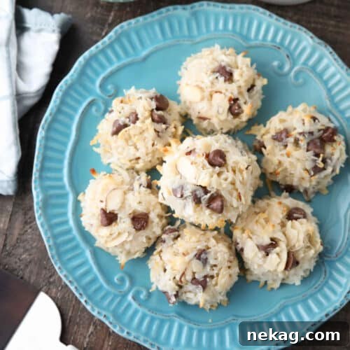Almond Joy Cookie Recipe with Coconut, Almonds & Chocolate Chips 10 Top view of Almond Joy Cookies (chocolate almond macaroons) on a plate with bowls of chocolate chips and sliced almonds on the side.