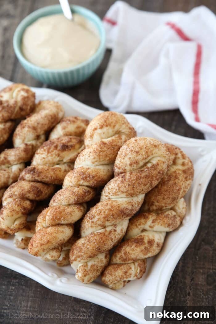 Cinnamon Twists Recipe: Crispy, Flaky Pastry with Sweet Glaze 3 Focus on plate of cinnamon breadsticks with bowl of cream cheese dip and a towel in the background.