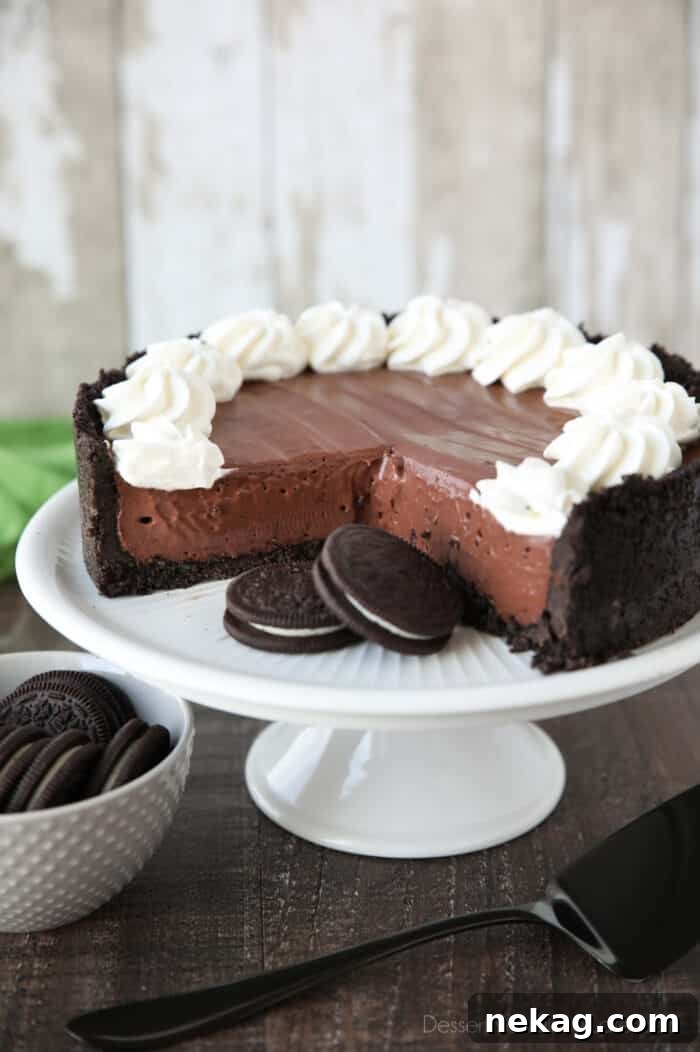 No-bake chocolate cheesecake and Oreos on a cake plate with whipped cream piped on top.