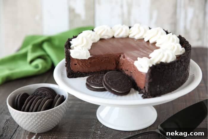 No bake chocolate cheesecake and Oreos on a cake plate with whipped cream piped on top.