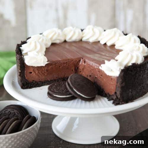 No-bake chocolate cheesecake and Oreos on a cake plate with whipped cream piped on top.