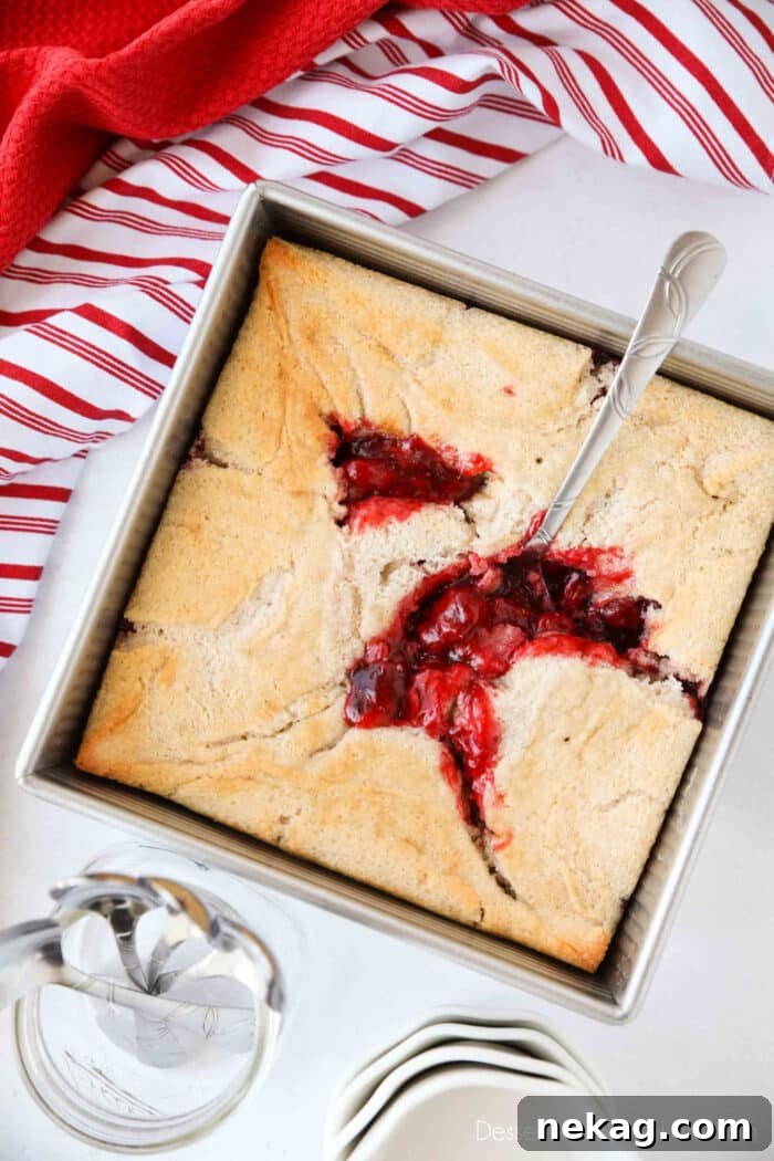 Classic Cherry Cobbler Recipe with Golden Biscuit Topping 4 Cherry Cobbler in a square baking pan with a spoon revealing cherry pie filling underneath the cake.