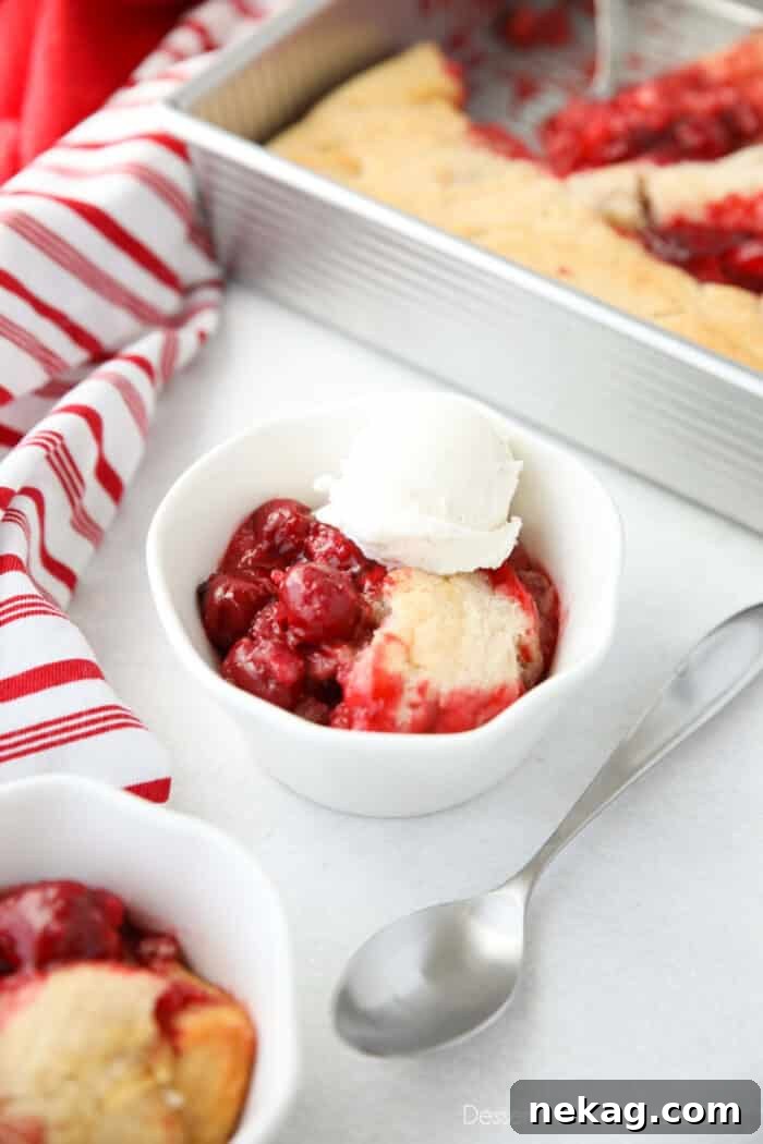Classic Cherry Cobbler Recipe with Golden Biscuit Topping 5 Cherry Cobbler in a bowl topped with vanilla ice cream and a spoon on the side.