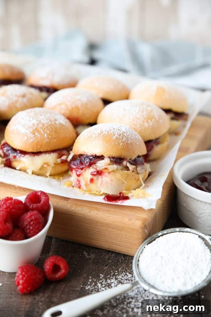 Crispy Monte Cristo Sliders with Ham, Turkey & Melty Cheese 2 Monte Cristo Sliders on parchment paper with ham, turkey, Swiss cheese, and raspberry preserves inside of dinner rolls with powdered sugar on top.