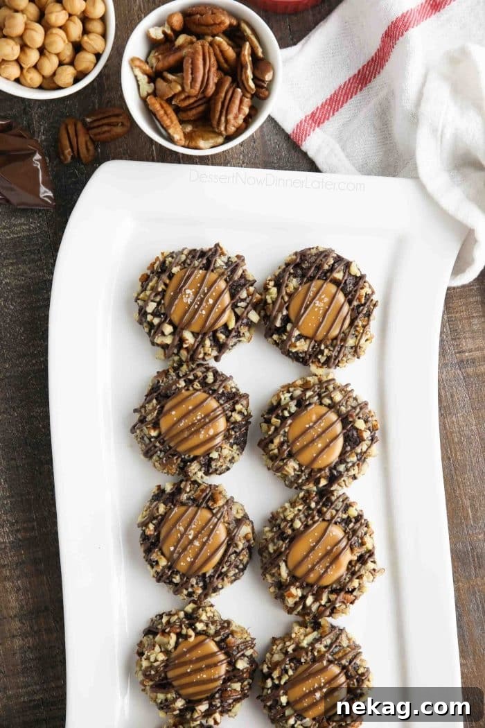 Long white plate of turtle thumbprint cookies with pecans and caramel bits nearby.