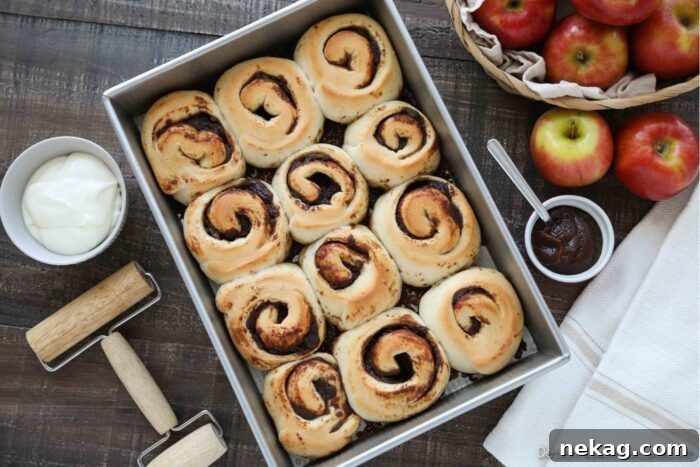 Baked Apple Butter Cinnamon Rolls in Pan with cream cheese glaze in a bowl on the side.