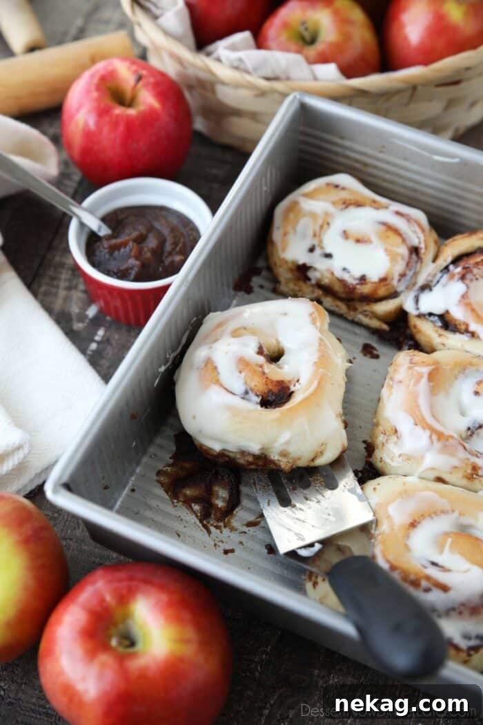 Scooping an apple butter cinnamon roll out of the pan with a spatula.
