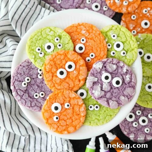 Bright colored Halloween cookies on a plate with powdered sugar cracks and candy eyeballs.