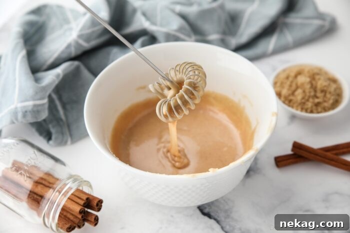 Cinnamon brown sugar glaze dripping off of a whisk into a bowl.