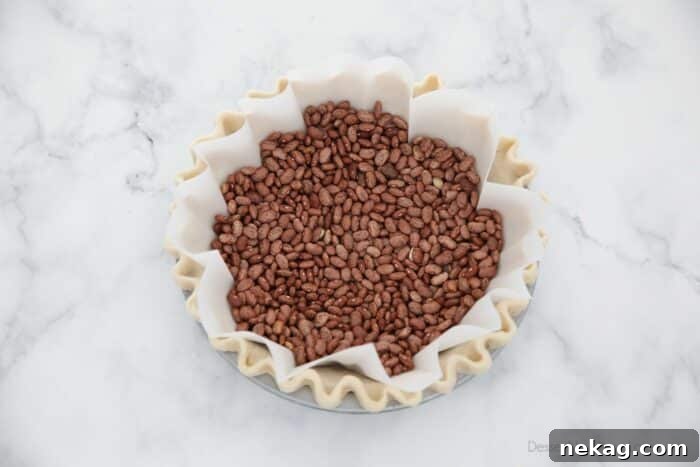 Parchment paper fitted in pie crust with dry beans on top for weights.