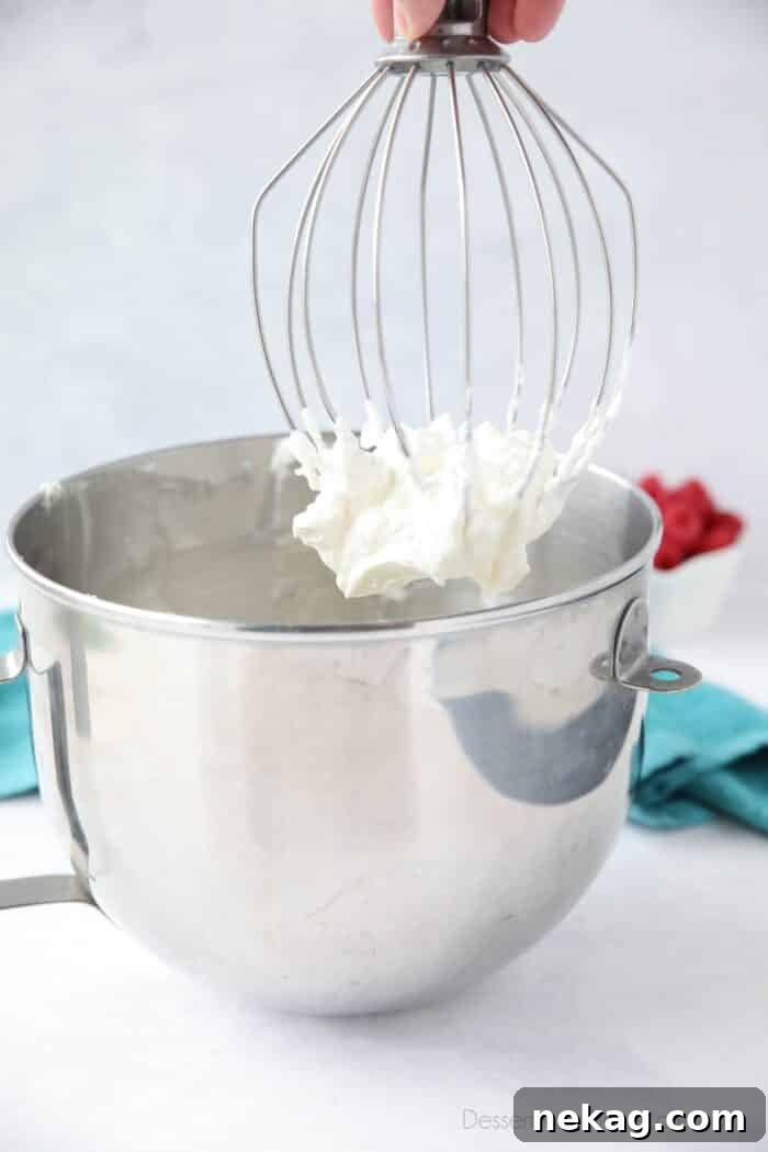 Pulling whisk attachment out of mixing bowl with whipped cream frosting on it.