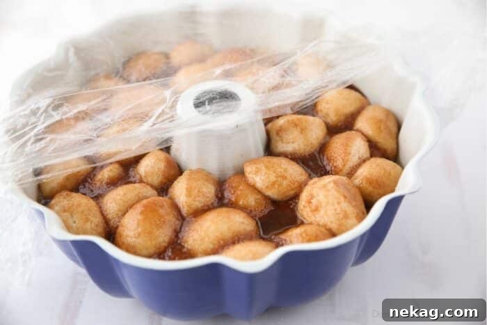 Soft Pull-Apart Monkey Bread Recipe with Video Tutorial 9 Monkey bread rising in pan with greased plastic wrap on top.