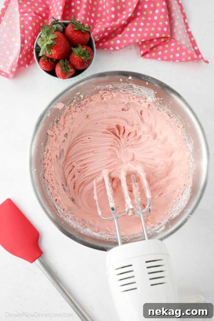 Strawberry cream cheese frosting in bowl with electric mixer and beaters.