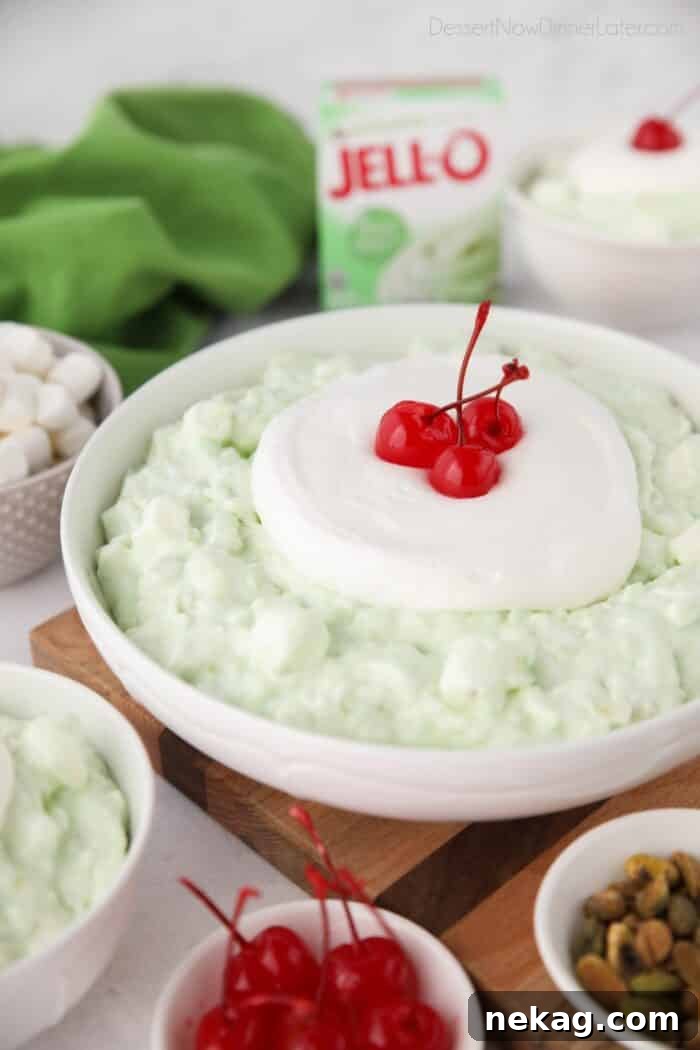 Big bowl full of pistachio fluff topped with whipped cream and maraschino cherries.