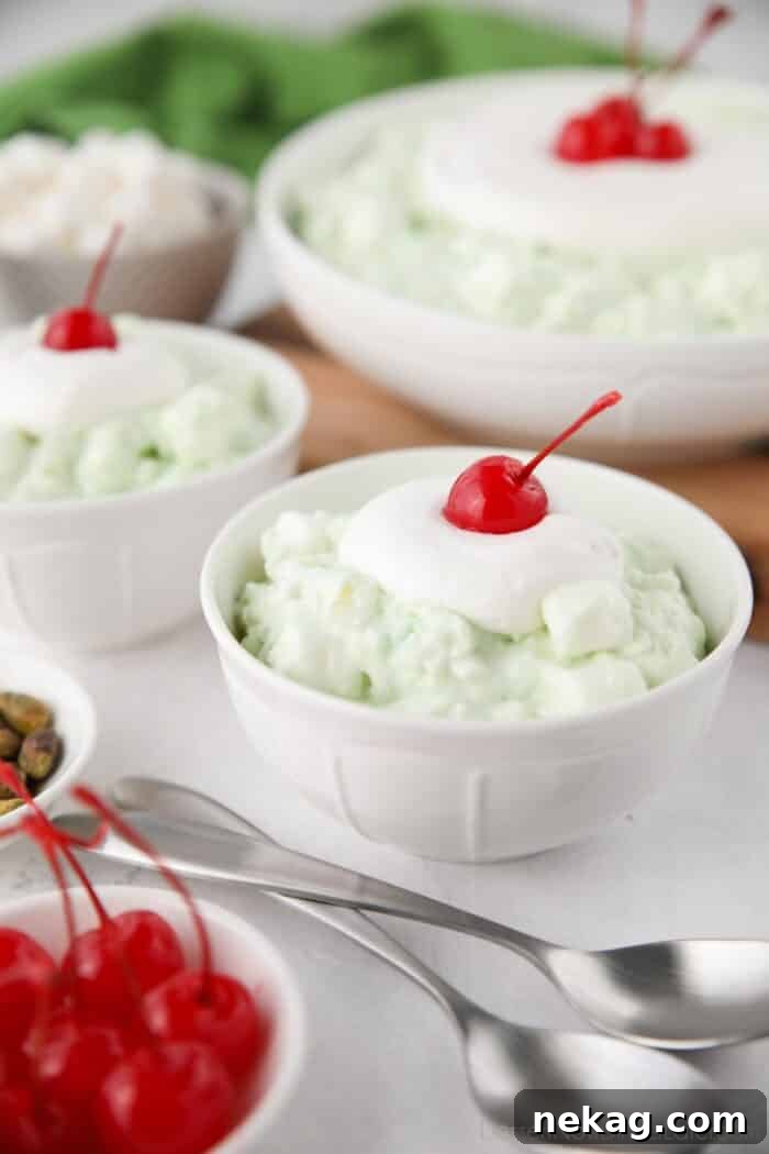 Bowls of watergate salad with whipped cream and cherries on top.