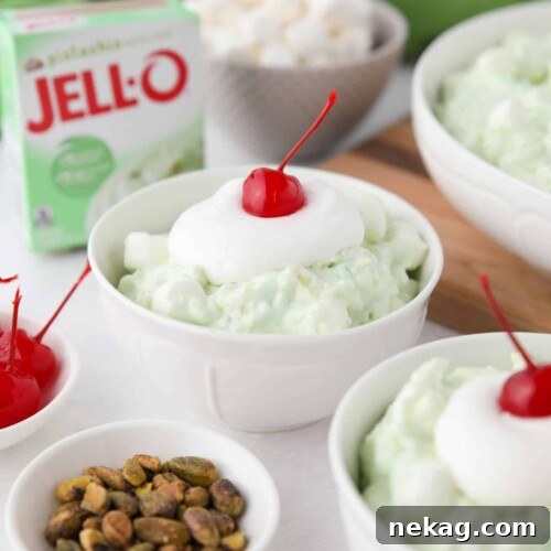 Close up of pistachio fluff in a bowl with whipped cream and a cherry on top.