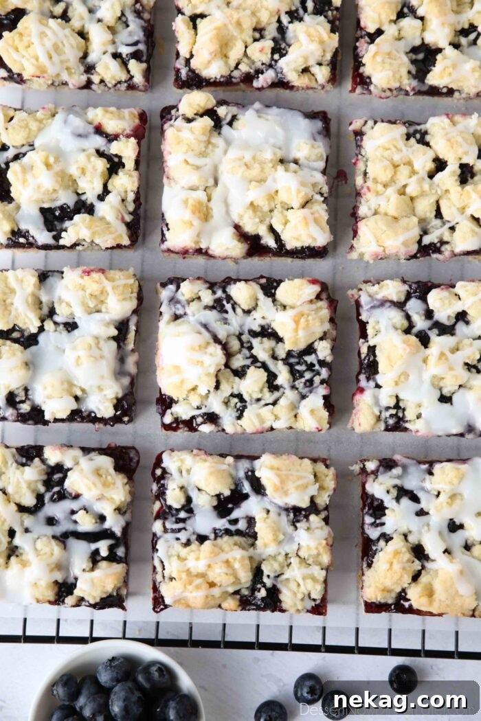 Blueberry Pie Bars Recipe — Rustic Layered Blueberry Dessert 3 Squares of blueberry pie bars with glaze on top resting on a cooling rack.