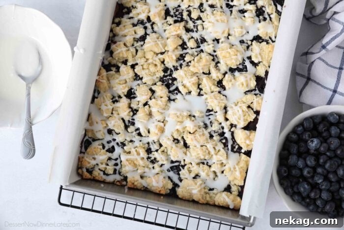 Blueberry Pie Bars Recipe — Rustic Layered Blueberry Dessert 5 Baked blueberry pie bars in a pan with glaze drizzled on top.