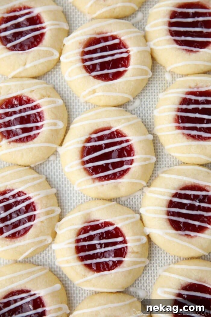 Icing drizzled on top of raspberry thumbprint cookies on a silicone baking mat.