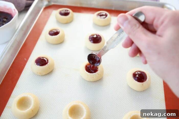 Spooning seedless raspberry jam into cookie wells.