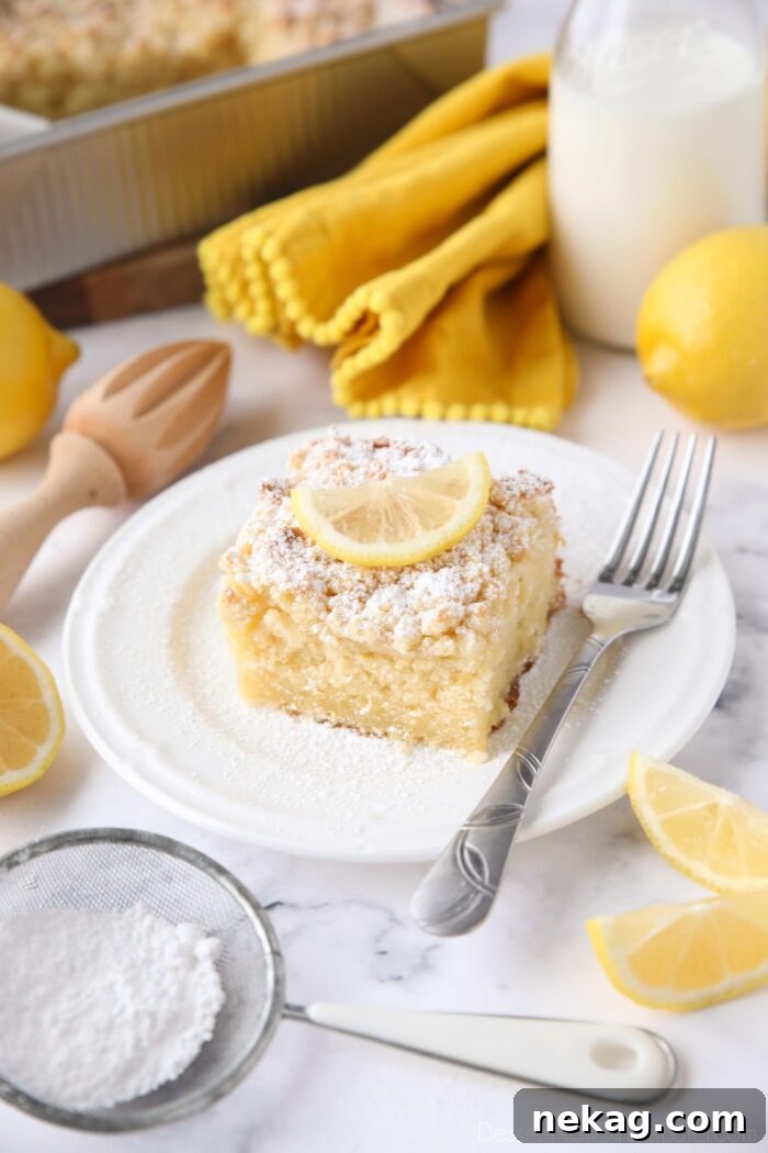 Thick slice of lemon coffee cake on a plate dusted with powdered sugar and a slice of lemon on top.