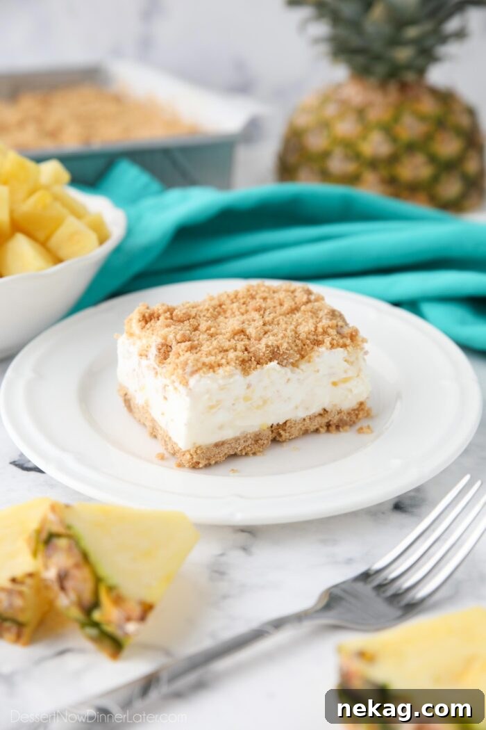 Side view of a slice of pineapple delight on a plate. A creamy pineapple dream dessert with buttery graham cracker crumbs.