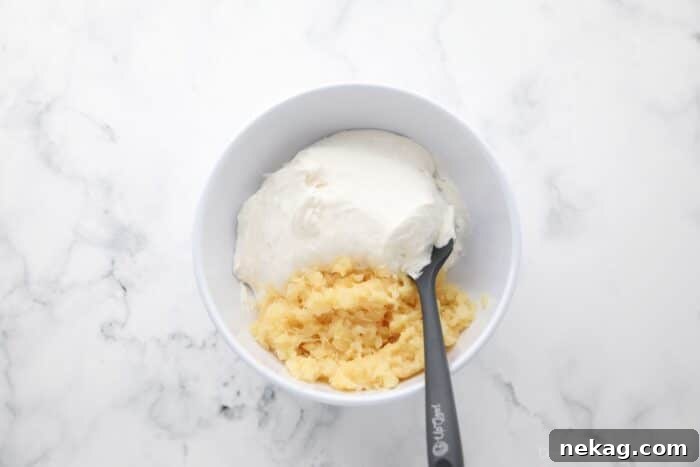 Folding crushed pineapple into whipped topping with a spatula.