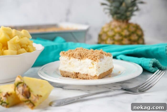 Square slice of pineapple delight on a plate consisting of a creamy pineapple filling sandwiched between graham cracker crumbs.