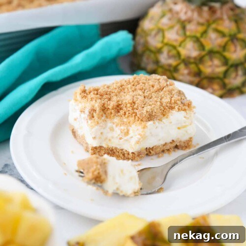 A slice of pineapple delight on a plate with a fork-full taken out. A creamy pineapple dream dessert with graham crackers, cream cheese, and whipped topping.