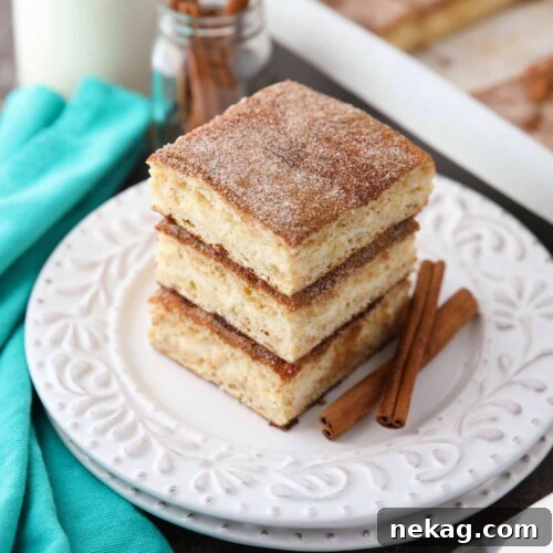Stack of sopapilla cheesecake bars on a plate with cinnamon sticks.