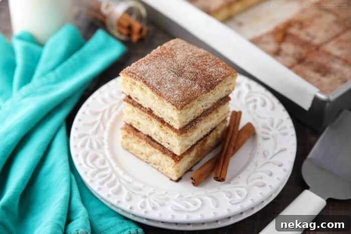 Stack of churro cheesecake bars on a plate with cinnamon sticks.