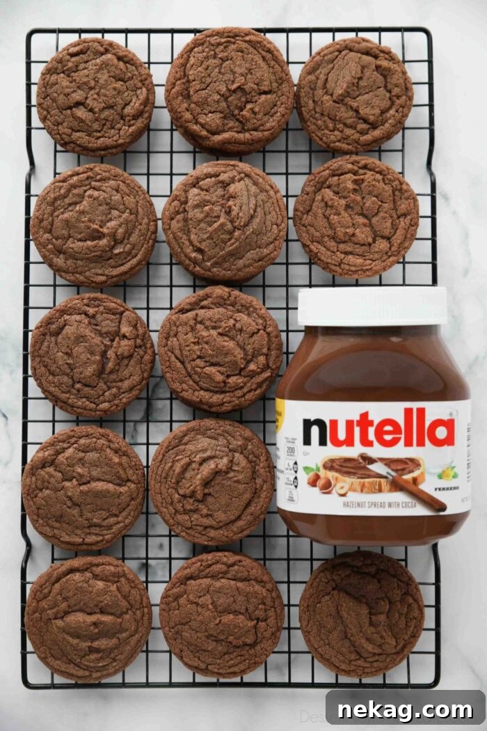 Decadent Nutella Cookie Recipe: Quick Homemade Chocolate Hazelnut Cookies 3 Nutella cookies on a wire cooling rack next to a jar of Nutella hazelnut spread with cocoa.