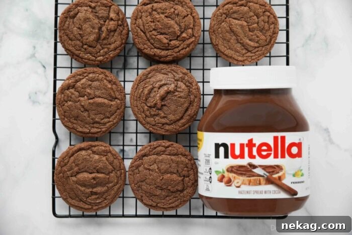 Decadent Nutella Cookie Recipe: Quick Homemade Chocolate Hazelnut Cookies 10 Jar of Nutella next to baked cookies on a wire cooling rack.