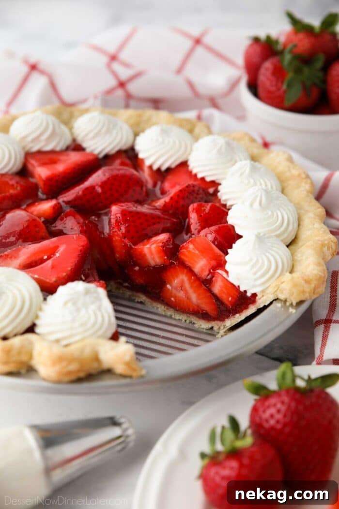 Fresh strawberry pie topped with whipped cream with a slice taken out of the pan.