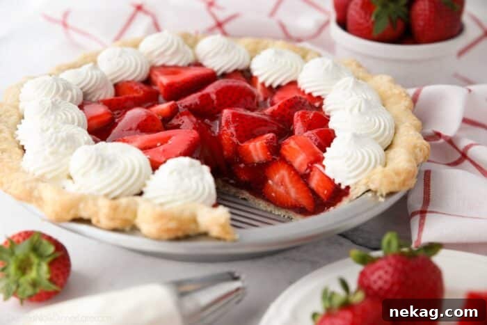 Fresh strawberry pie topped with whipped cream with a slice taken out of the pan.