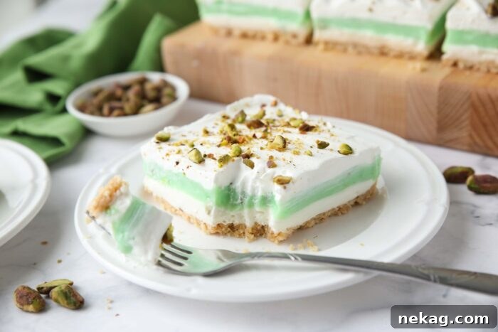 Decadent Pistachio Dessert Recipes to Impress Guests 11 Layered pistachio dessert on a plate with a fork-full taken out.