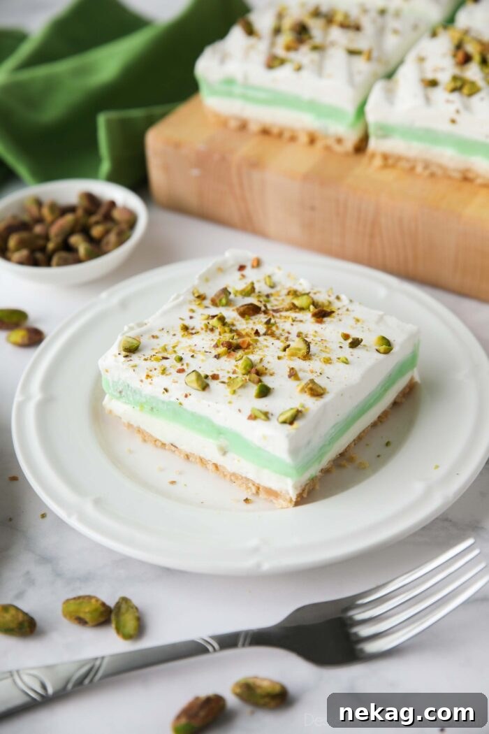 Decadent Pistachio Dessert Recipes to Impress Guests 4 Layered dessert with a shortbread cookie crust, no-bake cheesecake layer, pistachio pudding layer, and whipped cream on top sprinkled with chopped pistachios.
