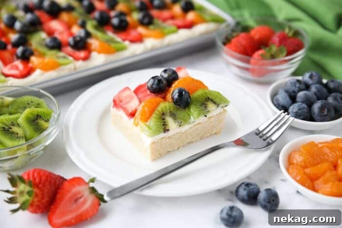 Square of sugar cookie fruit pizza on a plate with a fork.