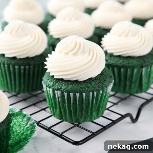 Cooling rack full of green cupcakes with whipped cream cheese frosting piped on top.