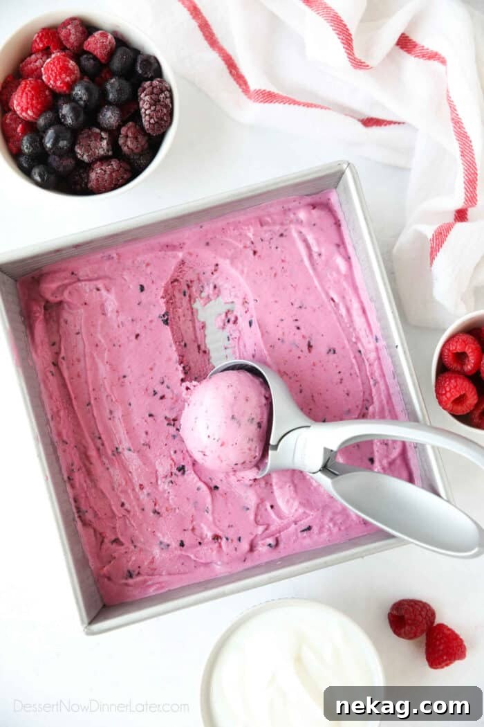 Homemade berry frozen yogurt in a shallow square dish being scooped with an ice cream scoop.