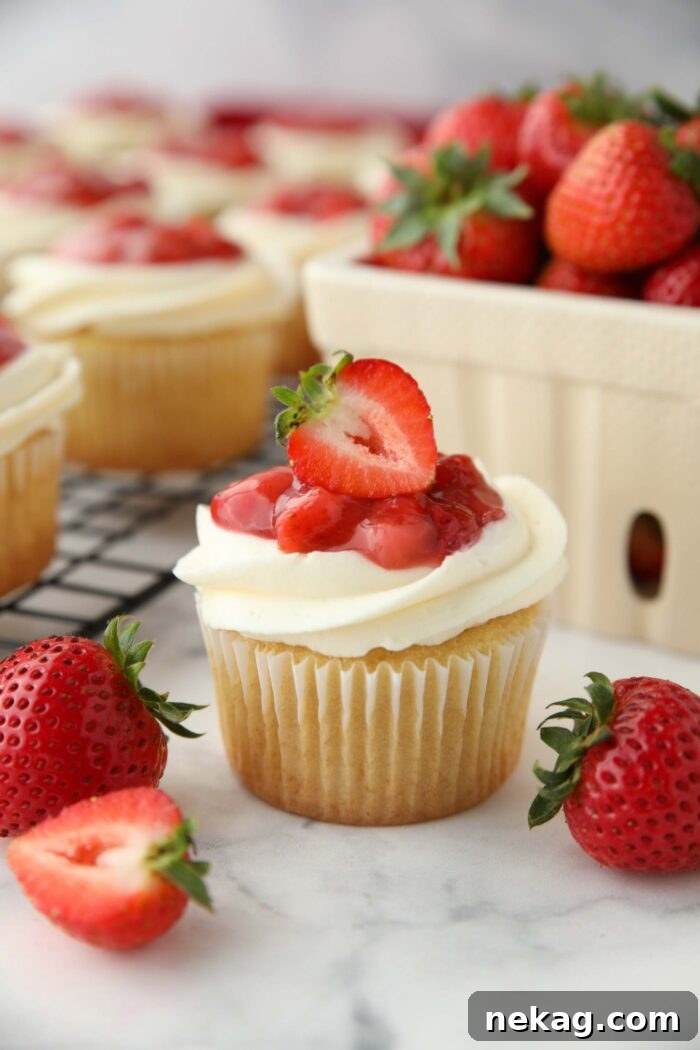 Strawberry Shortcake Cupcakes Recipe — Moist Strawberry Cupcakes 2 Close up of a Strawberry Shortcake Cupcake with vanilla cake, whipped cream cheese frosting, and strawberry sauce on top with a strawberry garnish.