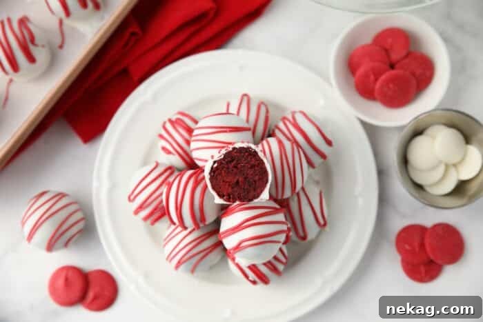 Red Velvet Truffle Recipe: Decadent Bite-Sized Chocolate Truffles 10 Red Velvet Truffles on a plate with one cut open showing the red cake inside of the white chocolate shell.