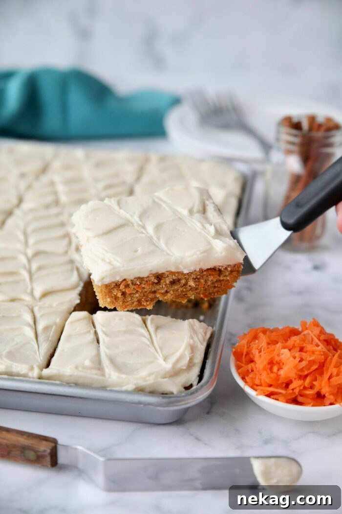 Carrot cake bars being scooped out of a sheet pan with a serving spatula.