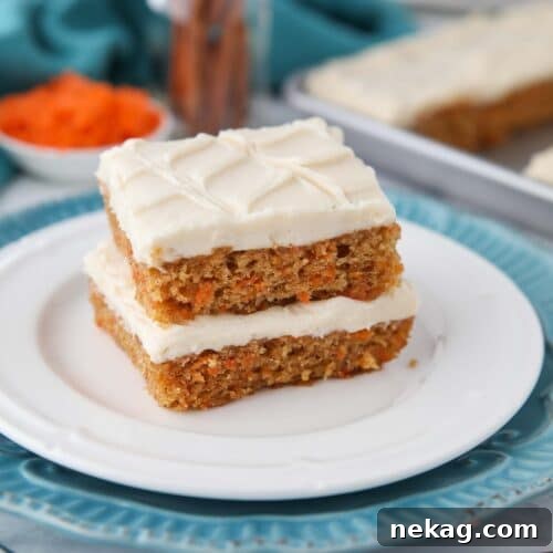 Two carrot cake bars with frosting stacked on a plate.