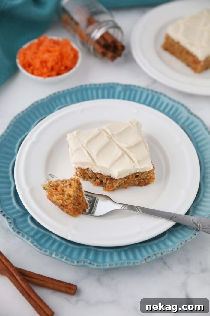 A single carrot cake bar with maple frosting on a plate with a forkful taken out.