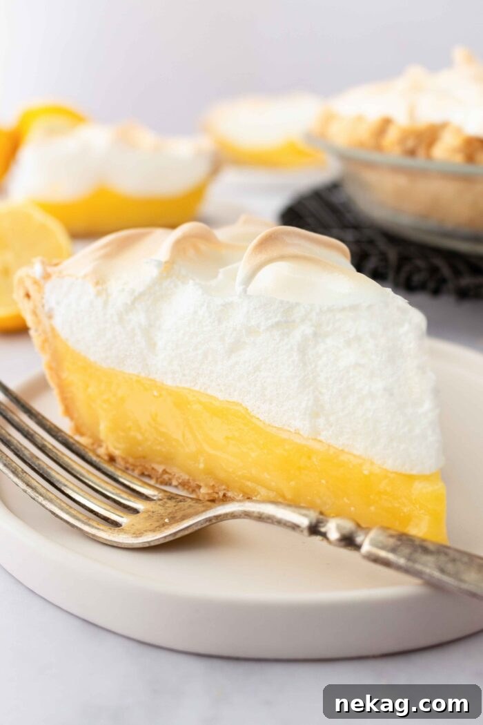 Classic Lemon Meringue Pie Recipe with Video Tutorial 4 Side view of a slice of lemon meringue pie on a plate showing layers of pastry crust, lemon filling, and meringue.