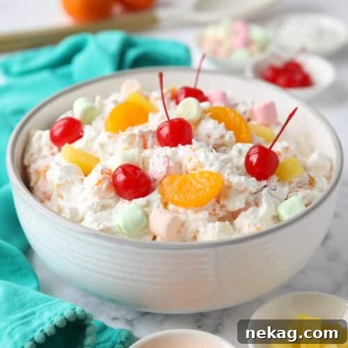 Bowl full of ambrosia salad with canned mandarin oranges, pineapple tidbits, maraschino cherries, shredded coconut, mini marshmallows, Greek yogurt and Cool Whip.
