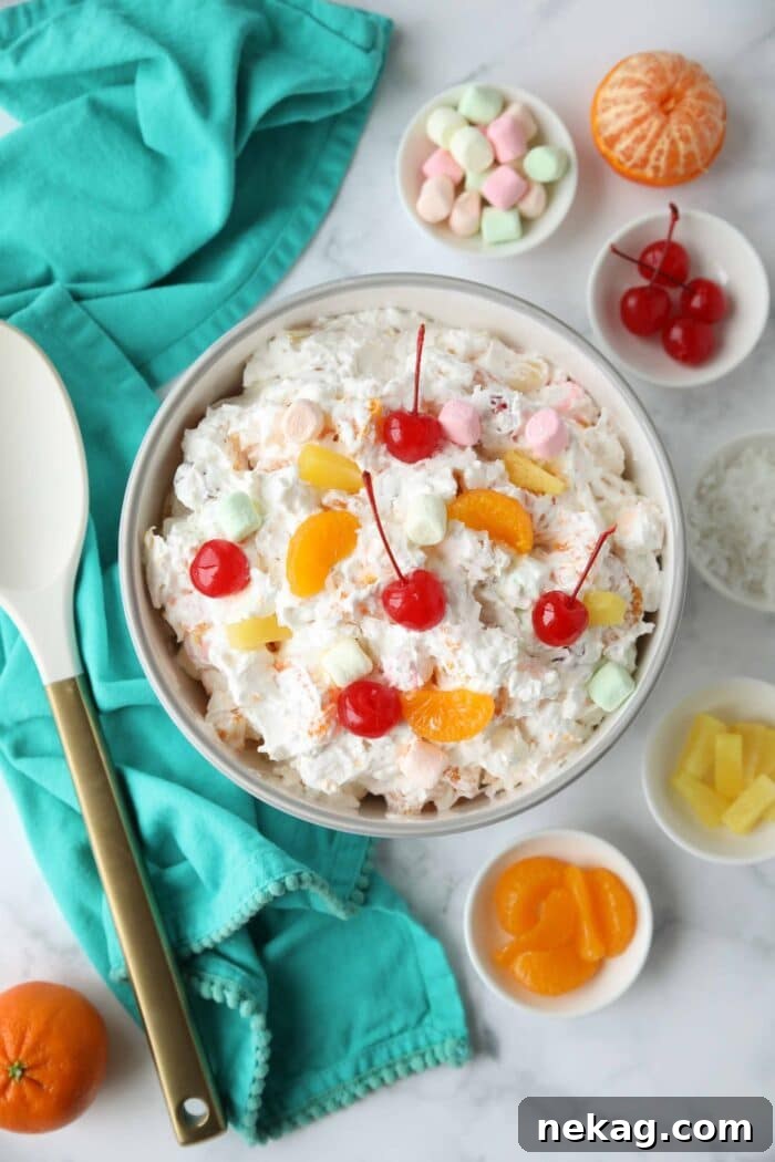 Top view of ambrosia salad in a bowl with canned mandarin oranges, pineapple tidbits, maraschino cherries, shredded coconut, mini marshmallows, Greek yogurt and Cool Whip.