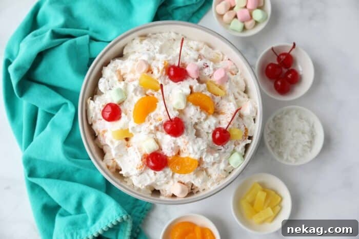 Top view of ambrosia fruit salad in a bowl with canned mandarin oranges, pineapple tidbits, maraschino cherries, shredded coconut, mini marshmallows, Greek yogurt and Cool Whip.